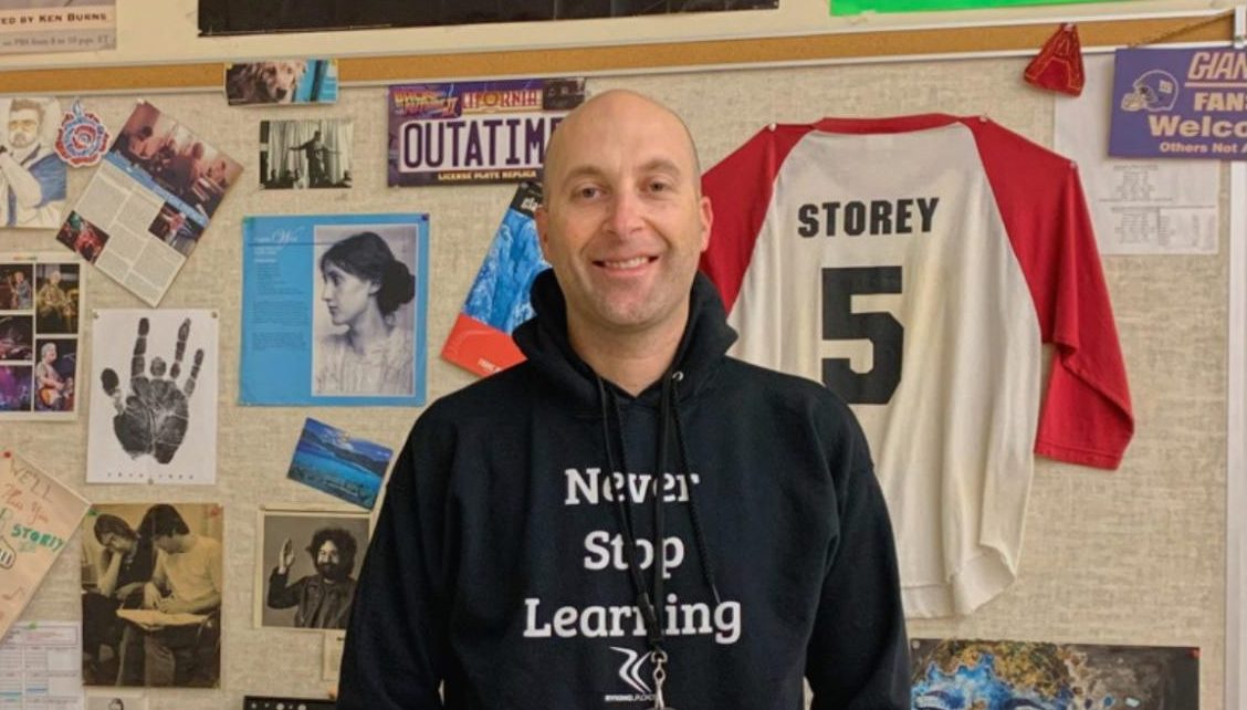 Mr. Storey poses next to his wall of memories in his classroom in F108.